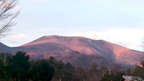 Une montagne à la pente douce et au sommet plat, entourée d’arbres et de quelques bâtiments.