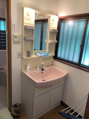 Une salle de bain avec un lavabo rose, un miroir, une fenêtre avec des rideaux, un porte-serviettes et une poubelle.