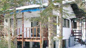 Une cabane en bois dotée d’un balcon, entourée d’arbres et recouverte de neige.
