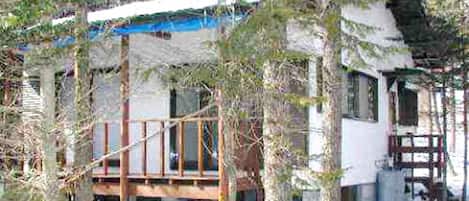 A wooden cabin with a balcony, surrounded by trees and covered with snow.