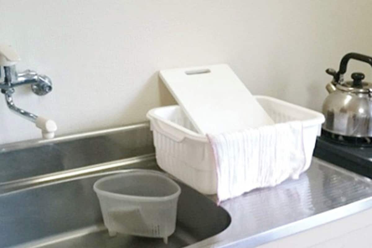 A kitchen sink with a kettle, a white basin, and a cup.