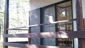 Une balustrade en bois orne un balcon, et une fenêtre donne sur une zone boisée.