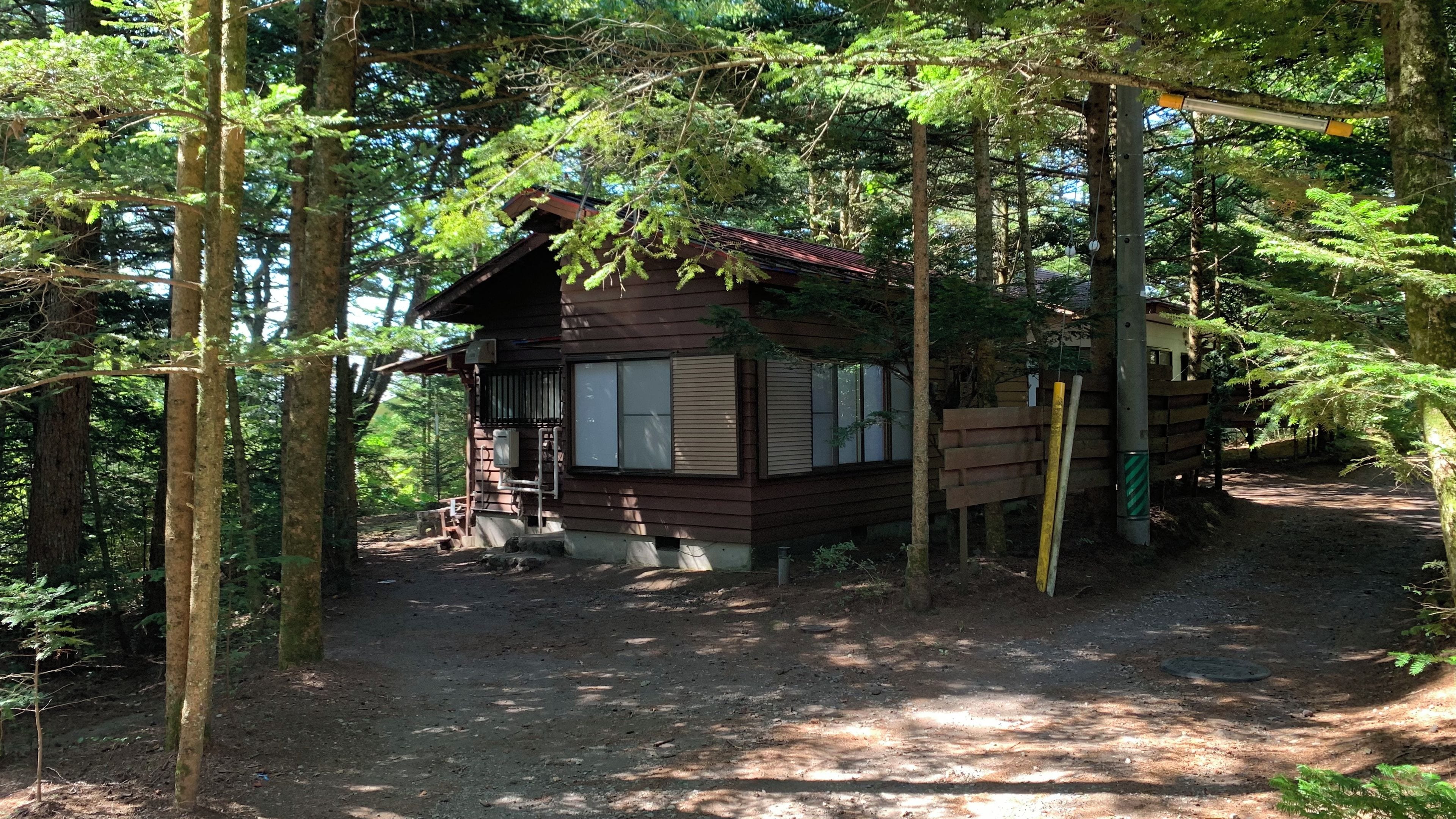 Uma cabana rodeada por árvores, com um caminho de terra que a leva até ela.