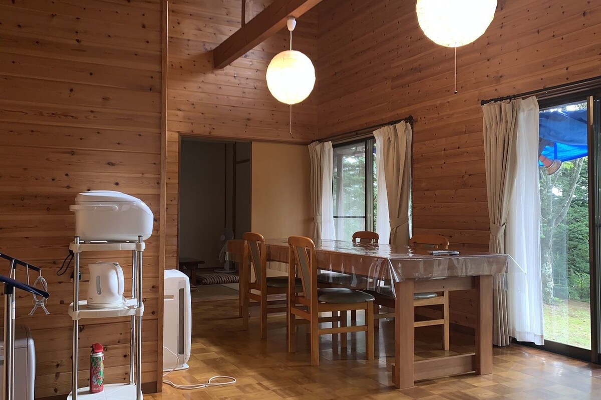 Una cabaña de madera con una mesa de comedor, sillas, un hervidor, un tostador y un dispensador de agua.