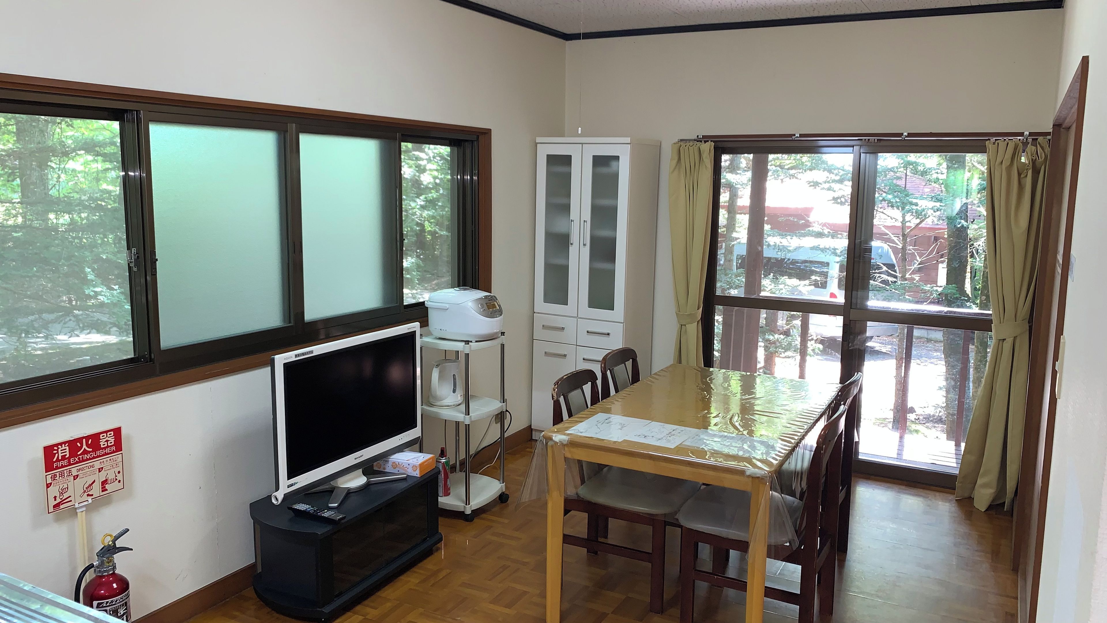 Quarto com televisão, um armário, mesa de jantar com cadeiras e extintor de incêndio.