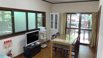 Quarto com televisão, um armário, mesa de jantar com cadeiras e extintor de incêndio.