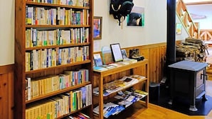 Een bibliotheek met boekenplanken, een tafel met leesvoer, een open haard en een houten trap.