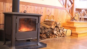 Een houtkachel met een stapel hout ernaast, houten wanden en een houten trap.