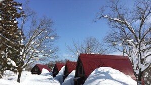 Une rangée de cabanes aux toits rouges, avec un sol enneigé et des arbres sans feuilles.