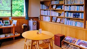 Une bibliothèque avec des étagères en bois, une table ronde entourée de chaises et un petit meuble.