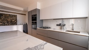 A modern kitchen with marble countertops, built-in appliances, and a stone accent wall. - Apartment in Lenno  Lake Como (Lenno)
