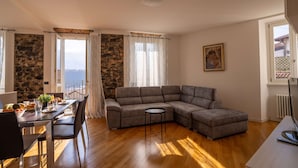 A living room with a gray sectional sofa, a dining table with chairs, a small round table, and a view through a window. - Apartment in Lenno  Lake Como (Lenno)