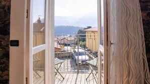 A view from a balcony with a metal railing, a white car parked in the background, and a stone wall on the left. - Apartment in Lenno  Lake Como (Lenno)