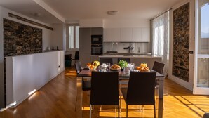 A modern kitchen with white cabinets, a stone accent wall, and a dining area with a table set for four. - Apartment in Lenno  Lake Como (Lenno)