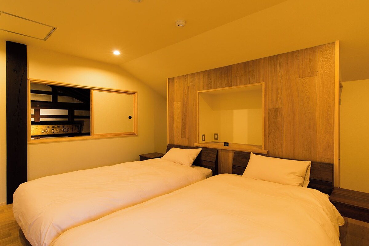 Een hotelkamer met twee bedden, houten hoofdborden, een grote spiegel en een plank met decoratieve spullen.