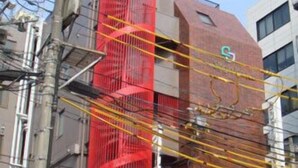A building with a prominent red cylindrical structure, likely a water tower, and a sign with a green 'S' on the side. - Single Inn Niigata No.2 (Niigata)