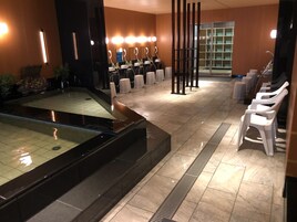 Un baño moderno con una fuente de agua central, varios lavamanos y una zona de estar con sillas blancas.