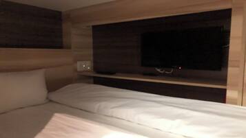 Una cama individual con ropa de cama blanca en una habitación con paredes de madera y un pequeño estante.