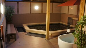 A traditional Japanese-style room with a wooden floor, a stone hot tub, a wooden bench, and a white bathtub. - Business Hotel Takami (Minamisoma)