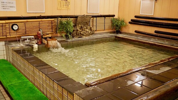 A traditional Japanese onsen with a stone bath, bamboo decorations, and a clock on the wall. - Business Hotel Takami (Minamisoma)