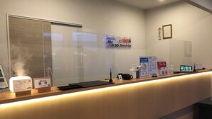 Un comptoir d’accueil d’hôtel avec un écran numérique, une enseigne indiquant « Mr. Kinjo Rent-A-Car » et une enseigne « Hotel One ».