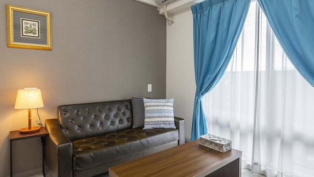 Un salon avec un canapé en cuir, une table basse en bois, une table d’appoint avec une lampe et un cadre photo accroché au mur.