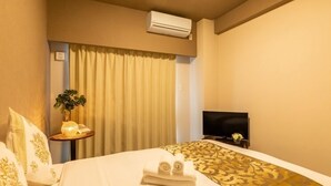 A hotel room with a bed, a TV, an air conditioner, a plant, and a window with curtains. - Mr. Kinjo in Mihara (Naha)