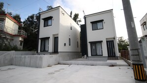 A modern two-story residential building with a flat roof, large windows, and a concrete driveway. - Akizero Onnason (Onna)