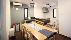 A compact kitchen with a dining area, featuring a wooden table, chairs, a microwave, and a built-in oven. - Akizero Onnason (Onna)