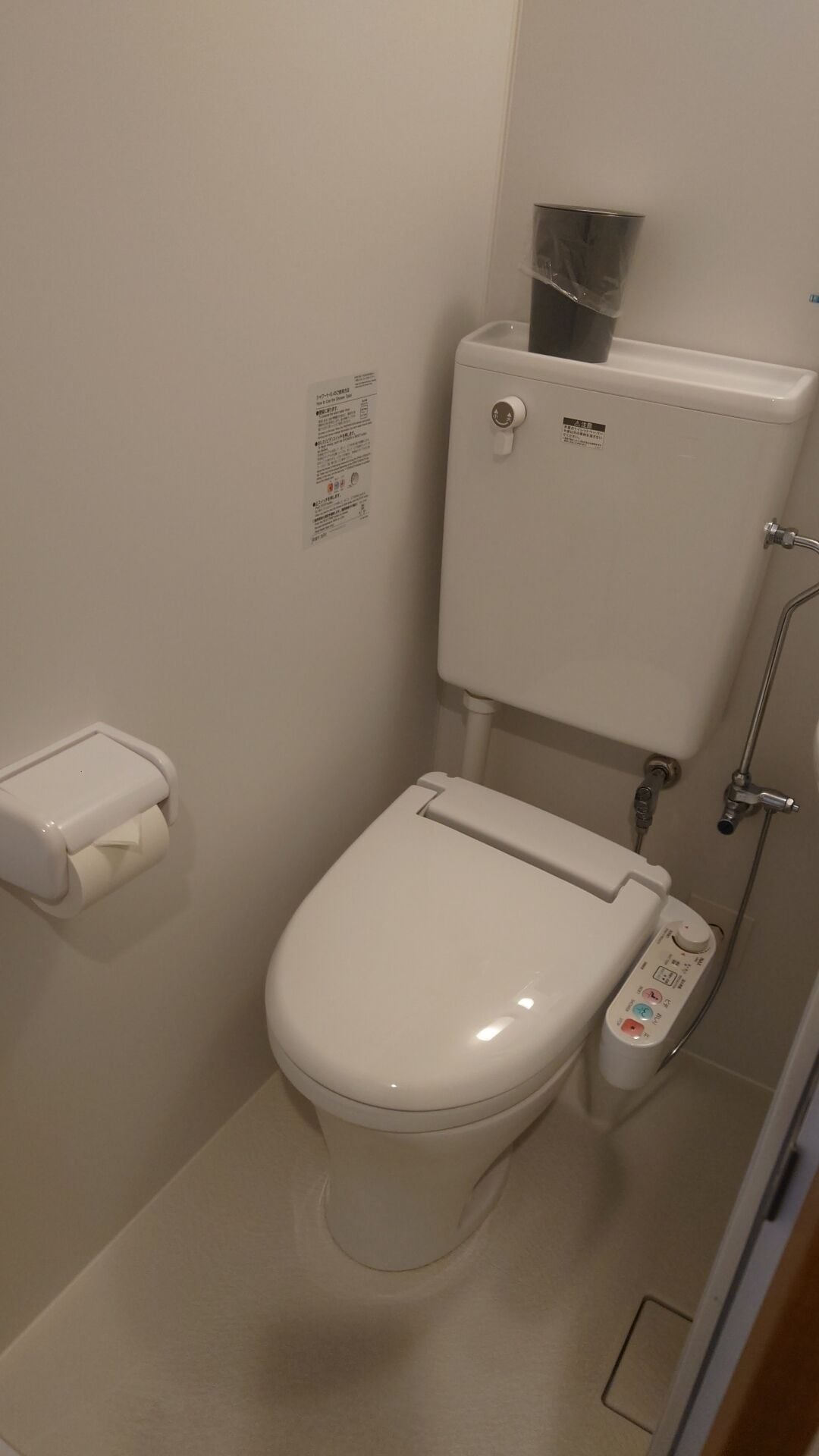 Une petite salle de bain moderne avec des toilettes blanches, un porte-rouleau de papier toilette, un bidet fixé au mur et un panneau de commande.