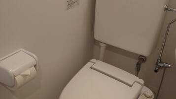Une petite salle de bain moderne avec des toilettes blanches, un porte-rouleau de papier toilette, un bidet fixé au mur et un panneau de commande.