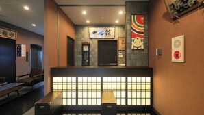 Een receptiegedeelte met een traditionele Japanse balie, een klok en een digitaal informatiebord.