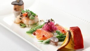 A white rectangular plate with a variety of food items including salmon, vegetables, and a piece of red fruit.