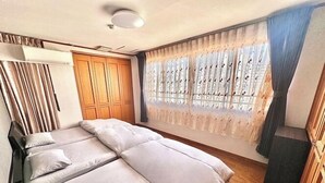 A bedroom with a double bed, wooden wardrobe, and a large window with curtains. - Maria Hotel (Utsunomiya)