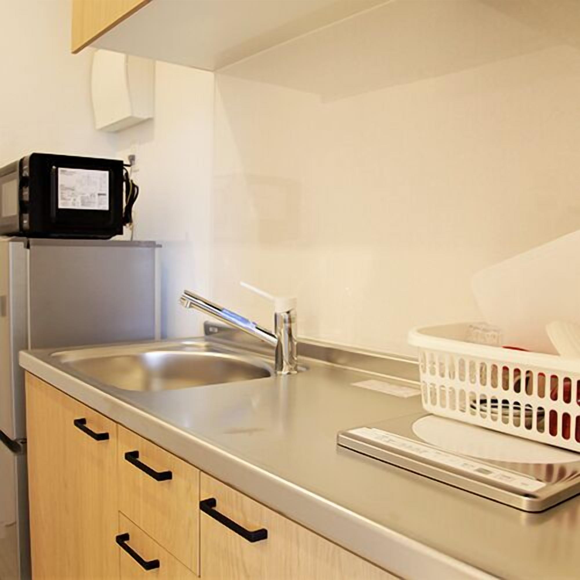 A kitchen with a stainless steel sink, wooden cabinets, a microwave, and a white laundry basket.