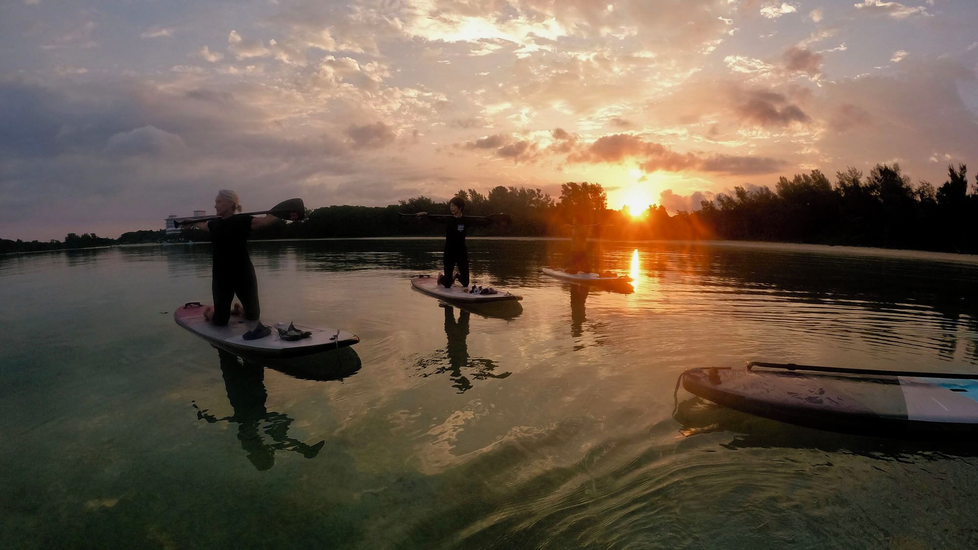 Duas pranchas de paddle em águas calmas, com um pôr do sol ao fundo.