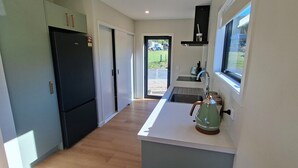 Una cucina moderna con un frigorifero nero, un bollitore verde e una finestra con vista su un giardino.