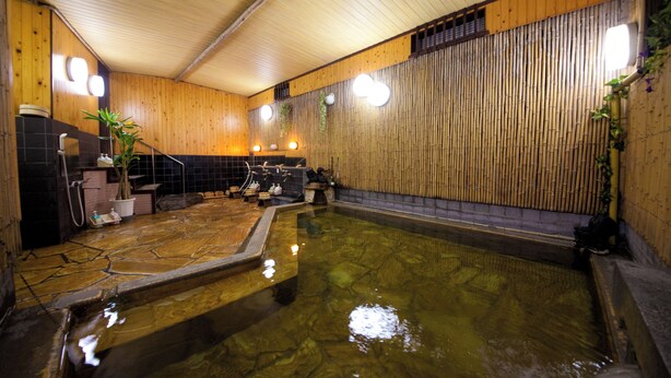 Um onsen japonês tradicional com interior em madeira, uma banheira de águas termais e uma pequena área de estar.