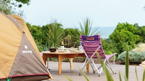 A tent labeled 'snow peeks' and a Coleman chair on a wooden deck with a table set for a meal, overlooking a lush landscape.