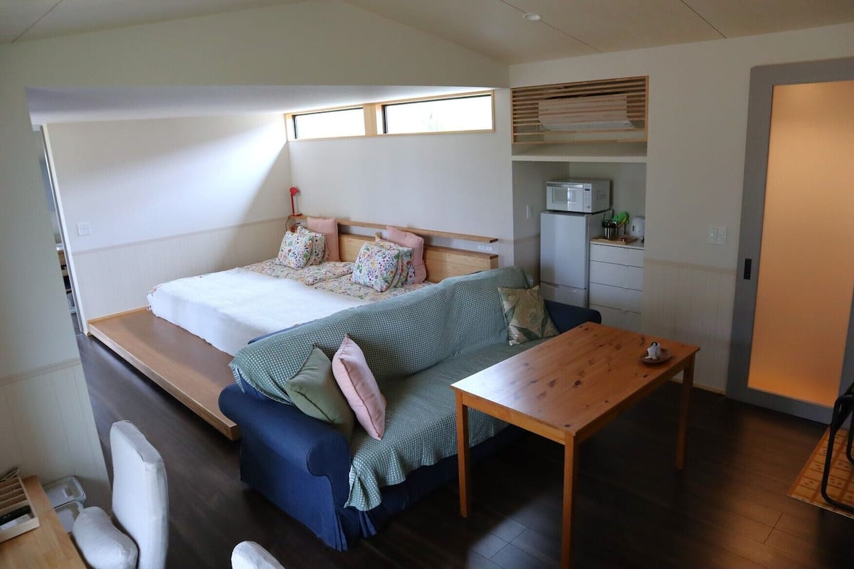 Quarto compacto com cama, sofá, mesa pequena e micro-ondas.