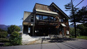 Une maison en bois à deux étages, dotée d’un balcon, de grandes fenêtres et d’un escalier menant à l’entrée.