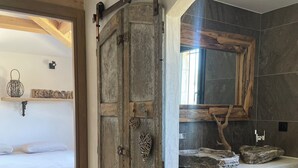 A room with a rustic wooden door, a bed with white bedding, a marble sink vanity, and a stone-tiled shower area. - Villa Luxury Lagoon - Aix en Provence (Ventabren)