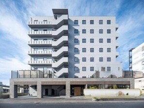 Un immeuble à plusieurs étages doté d’une architecture moderne, avec des balcons à chaque niveau et un espace d’entrée abrité.
