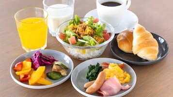 A table with various breakfast items including a bowl of salad, a plate of eggs, a plate of ham, a glass of orange juice, a cup of coffee, and a glass of milk.