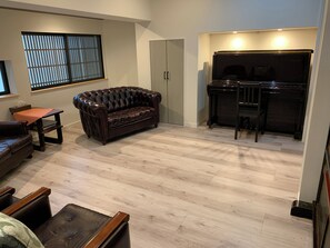 Una sala de estar con un sofá de cuero marrón oscuro, una mesa de centro de madera y un piano.