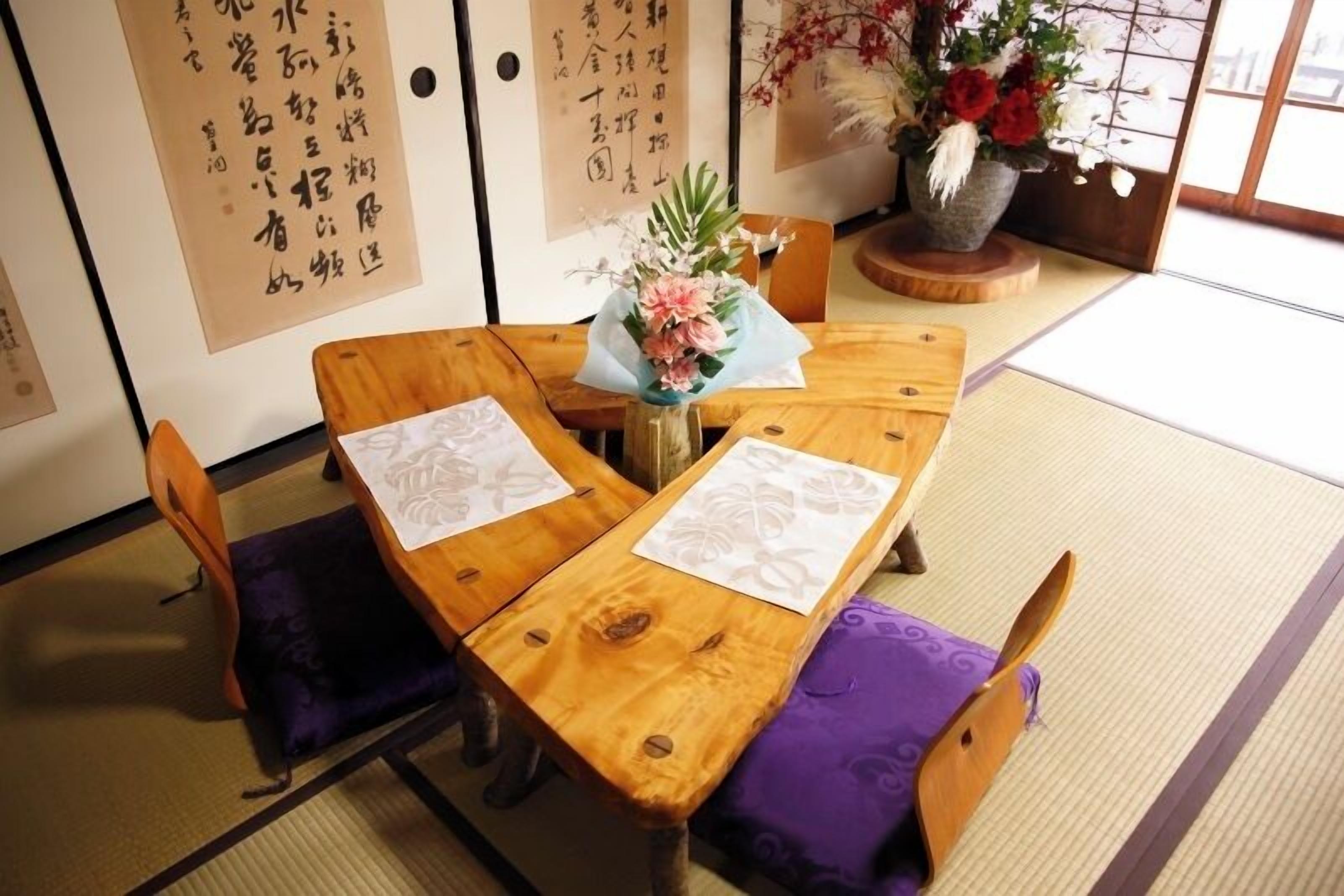 Ein traditioneller japanischer Raum mit Tatami-Boden, einem Holztisch mit violetten Kissen und Kalligraphie an den Wänden.