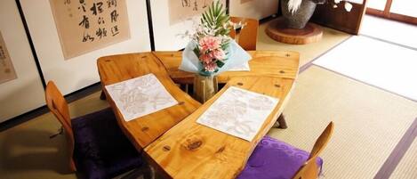 Ein traditioneller japanischer Raum mit Tatami-Boden, einem Holztisch mit violetten Kissen und Kalligraphie an den Wänden.