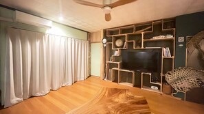 A living room with a flat-screen TV, wooden shelving, a clock, and a ceiling fan. - Komorebi (Miyakojima)