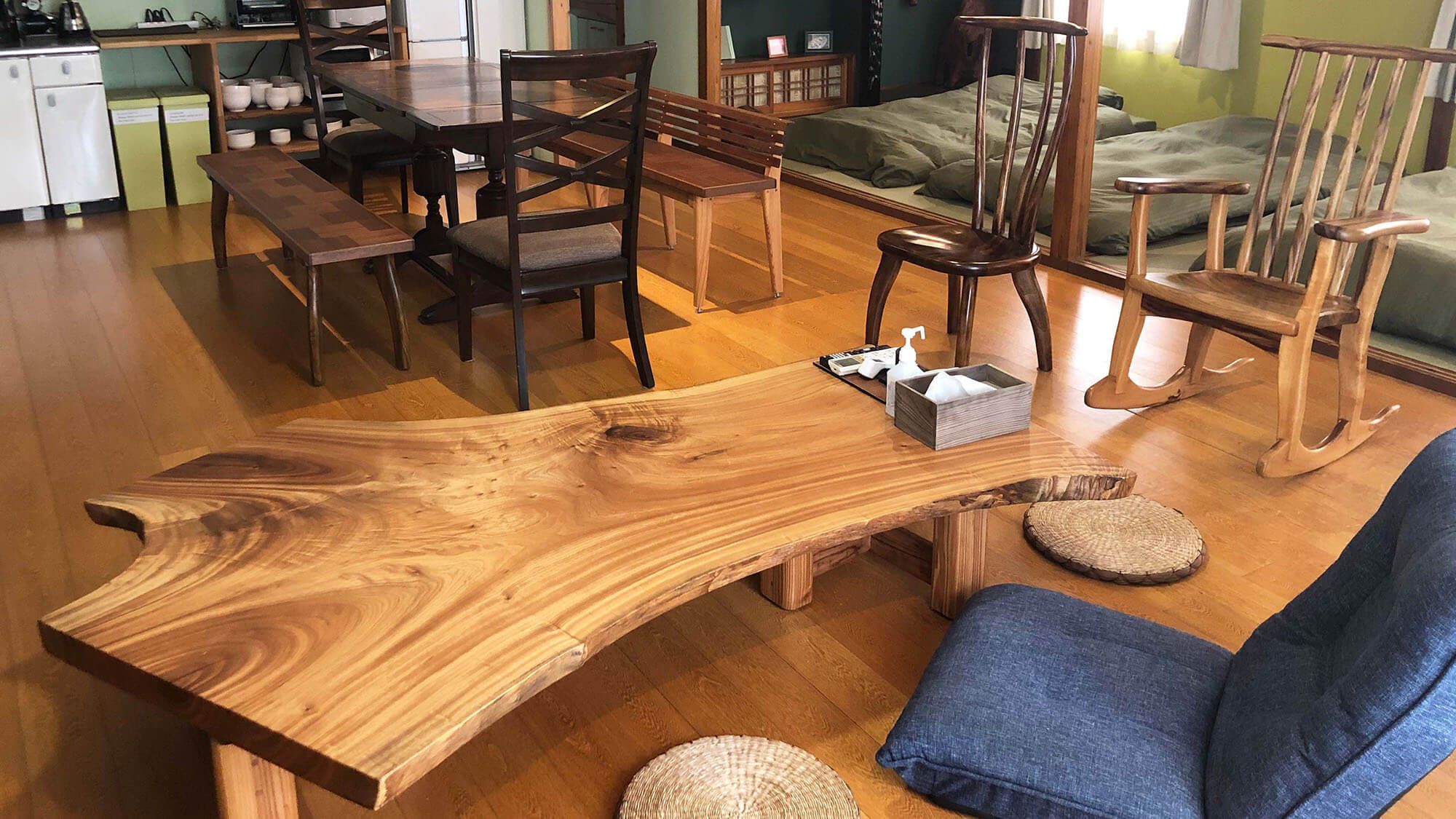 A room with a large wooden table, several chairs, a sofa, and a bed.