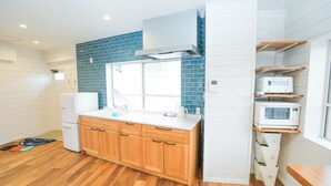A modern kitchen with wooden cabinets, a white countertop, a blue-tiled backsplash, and built-in microwave shelves. - Casablanca Vacation House (Tokunoshima)
